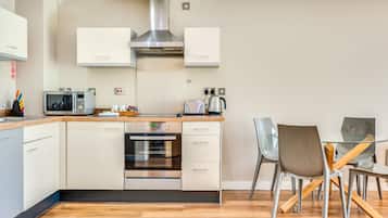 A modern kitchen with a built-in oven, microwave, and a stainless steel range hood. There is a glass dining table with chairs and a wooden chair.