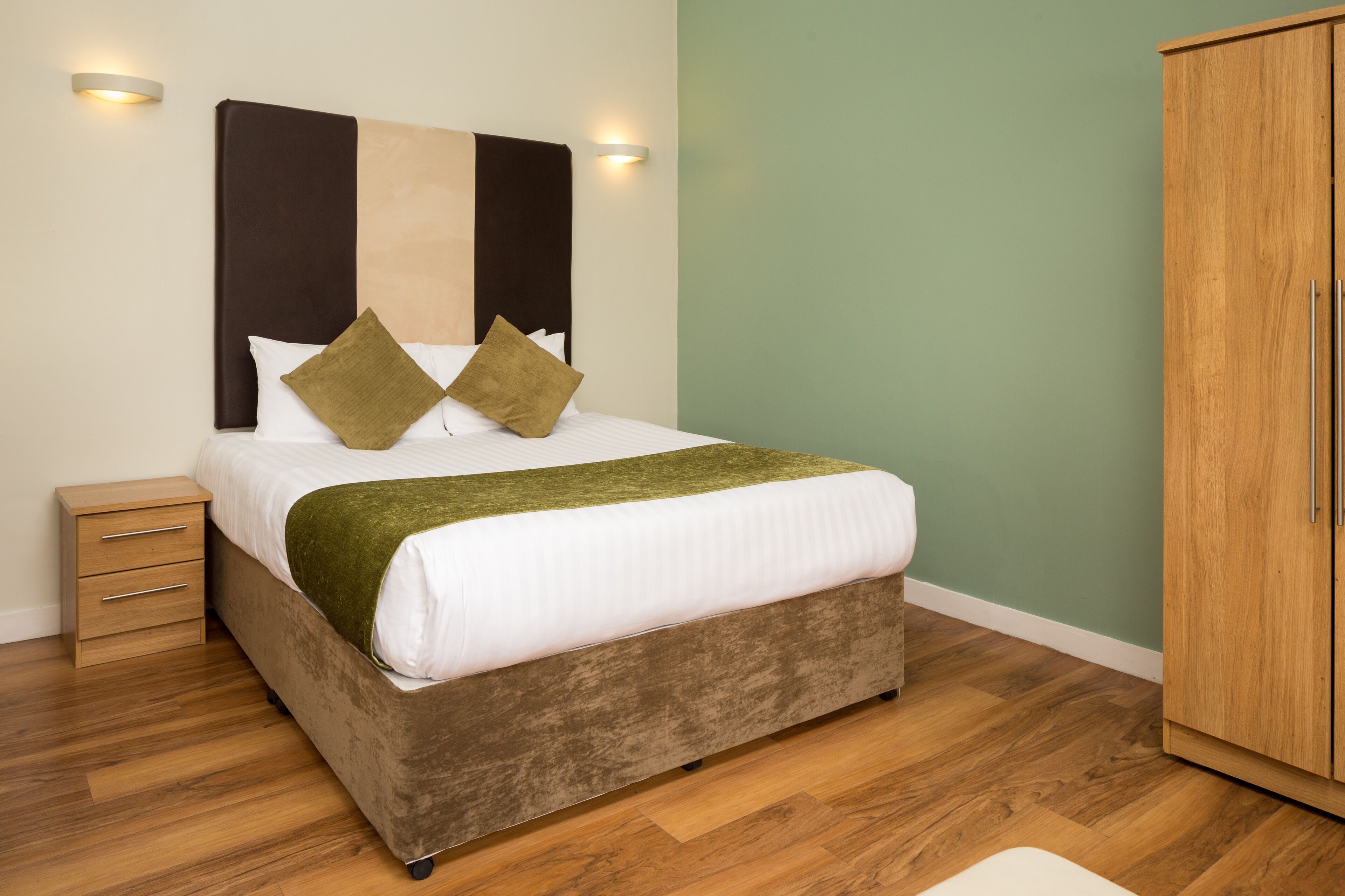 Una cama con cabecera, una mesita de noche y un armario en una habitación con suelo de madera.