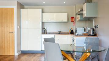 A modern kitchen with white cabinets, a glass dining table, and a wooden door.