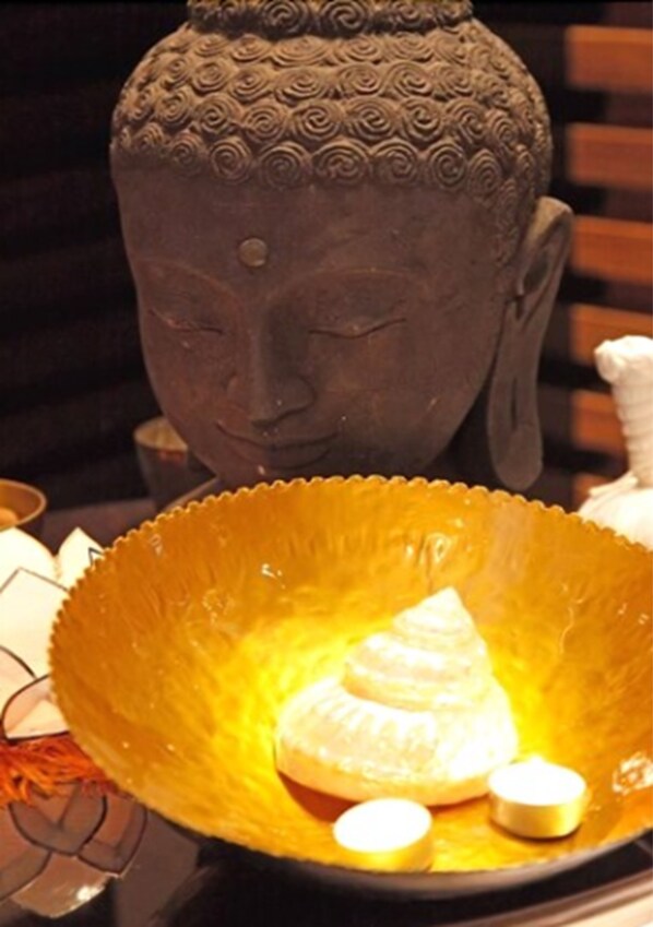 Una estatua de Buda con un adorno estampado en la parte superior y un cuenco con velas al frente.