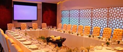 A long conference table with chairs, a projector screen, and a decorative wall.