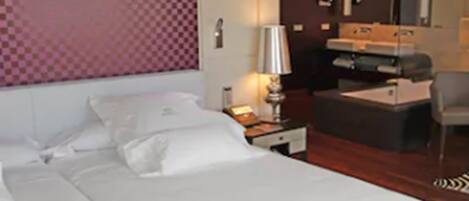 Una habitació d'hotel amb un llit gran, una taula de treball, una cadira i una taula petita.