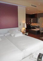 A hotel room with a large bed, a desk, a chair, and a small table.