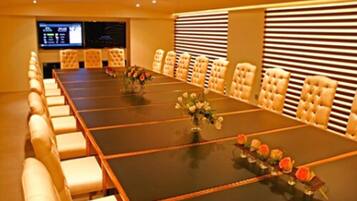 A conference room with a long table, multiple chairs, and a screen displaying information.