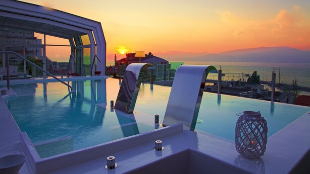 Een overloopzwembad met uitzicht op de zonsondergang boven de zee, een loungegedeelte met stoelen en een decoratieve lantaarn.