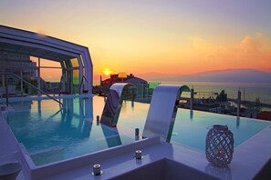 Una piscina infinita con vistas a la puesta de sol sobre el mar, un área de descanso con sillas y un farol decorativo.