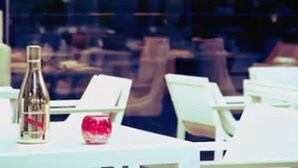 Een eethoek met witte tafels en stoelen, een fles en een rood voorwerp op tafel.