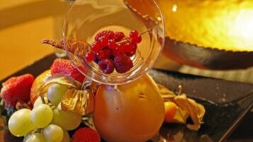 A glass containing red berries, grapes, and a slice of orange on a table with a dark surface.