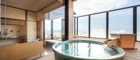 A modern interior with a large hot tub, wooden flooring, and large windows offering a city view.