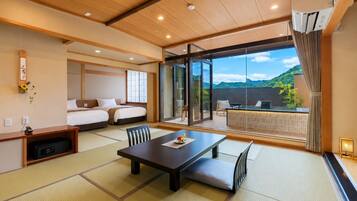 A modern hotel room with tatami flooring, a large sliding glass door to a balcony, and a view of a mountainous landscape.