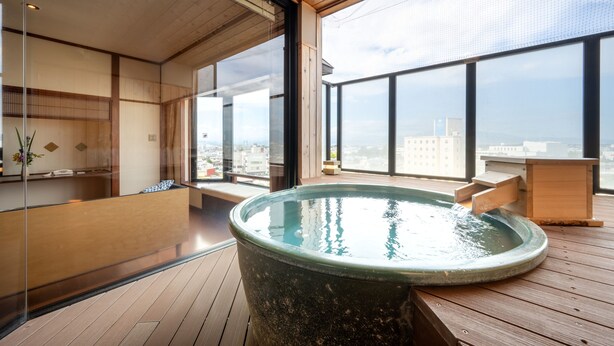 A modern spa area with a large hot tub, wooden flooring, and large windows offering city views. - Tendo Onsen TAKINOYU (Tendo)