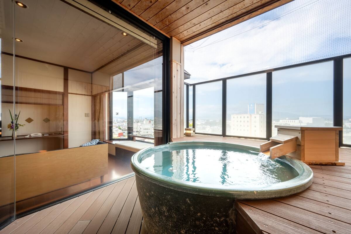 Ett modernt spaområde med en stor bubbelpool, trägolv och stora fönster med utsikt över staden.