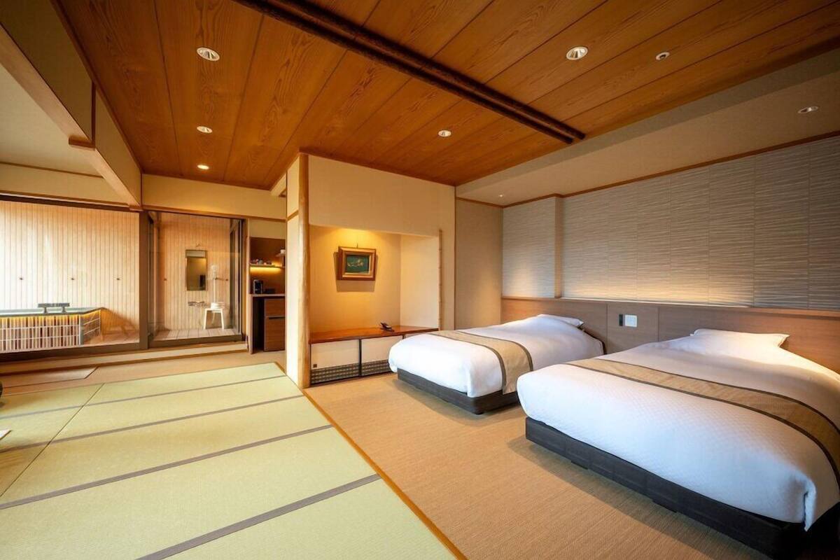Ett hotellrum med två sängar, ett träpanelat tak, ett golv täckt av tatamimattor och en skjutdörr som leder ut till en balkong.