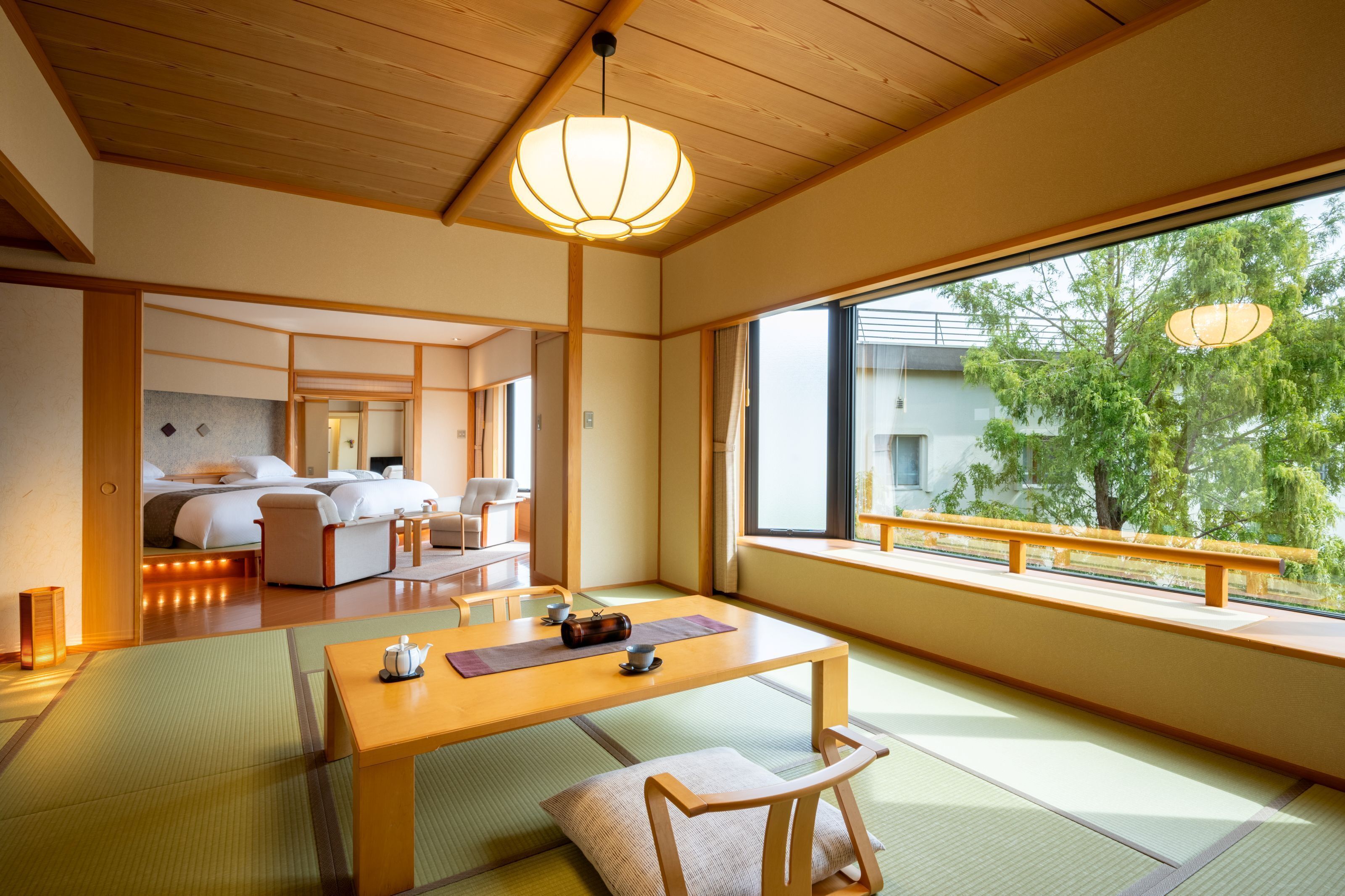 A traditional Japanese-style room with tatami flooring, a low wooden table, and a view of greenery outside.