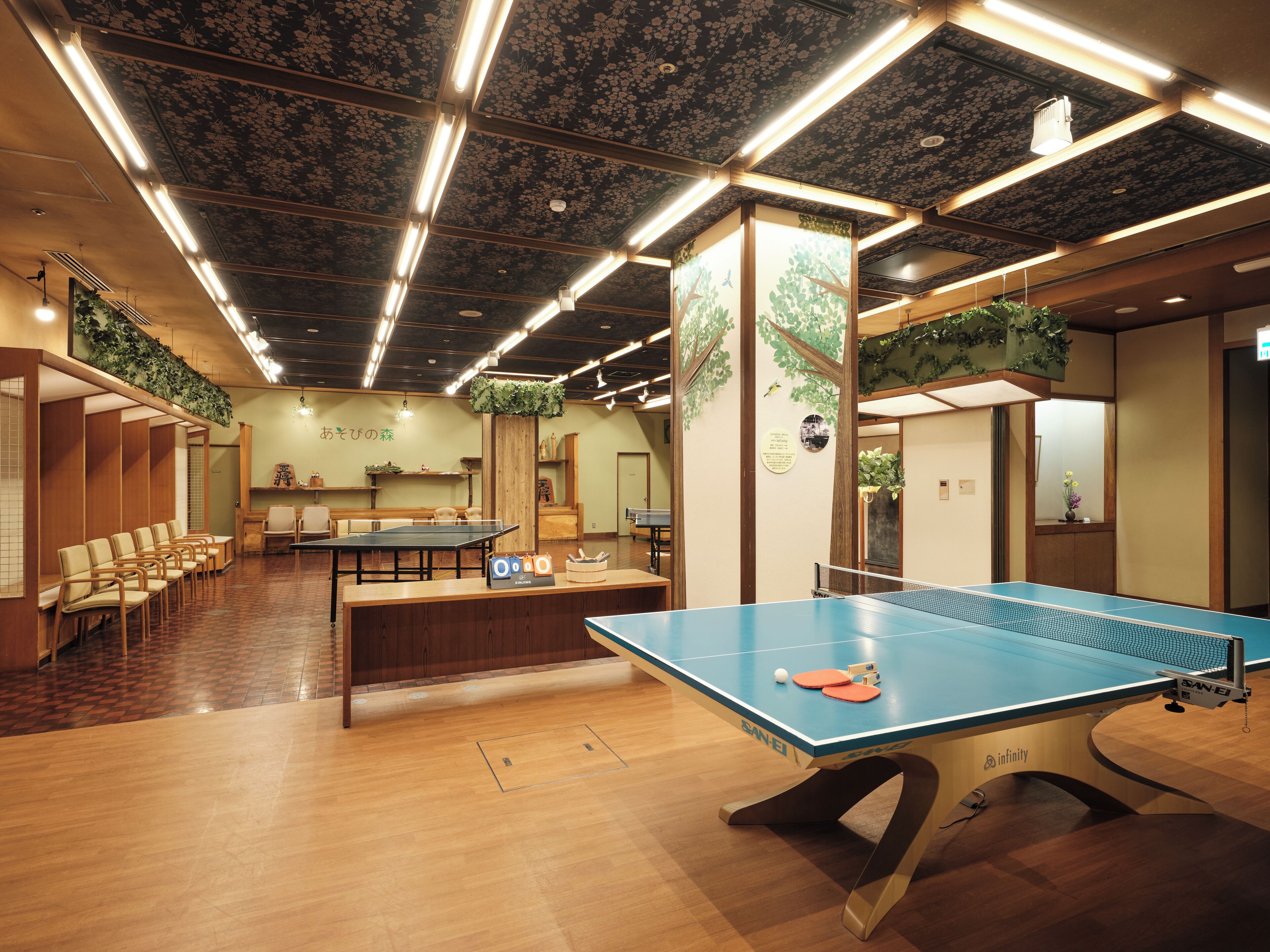 Una mesa de ping pong en una habitación con piso de madera y techo con diseños florales.