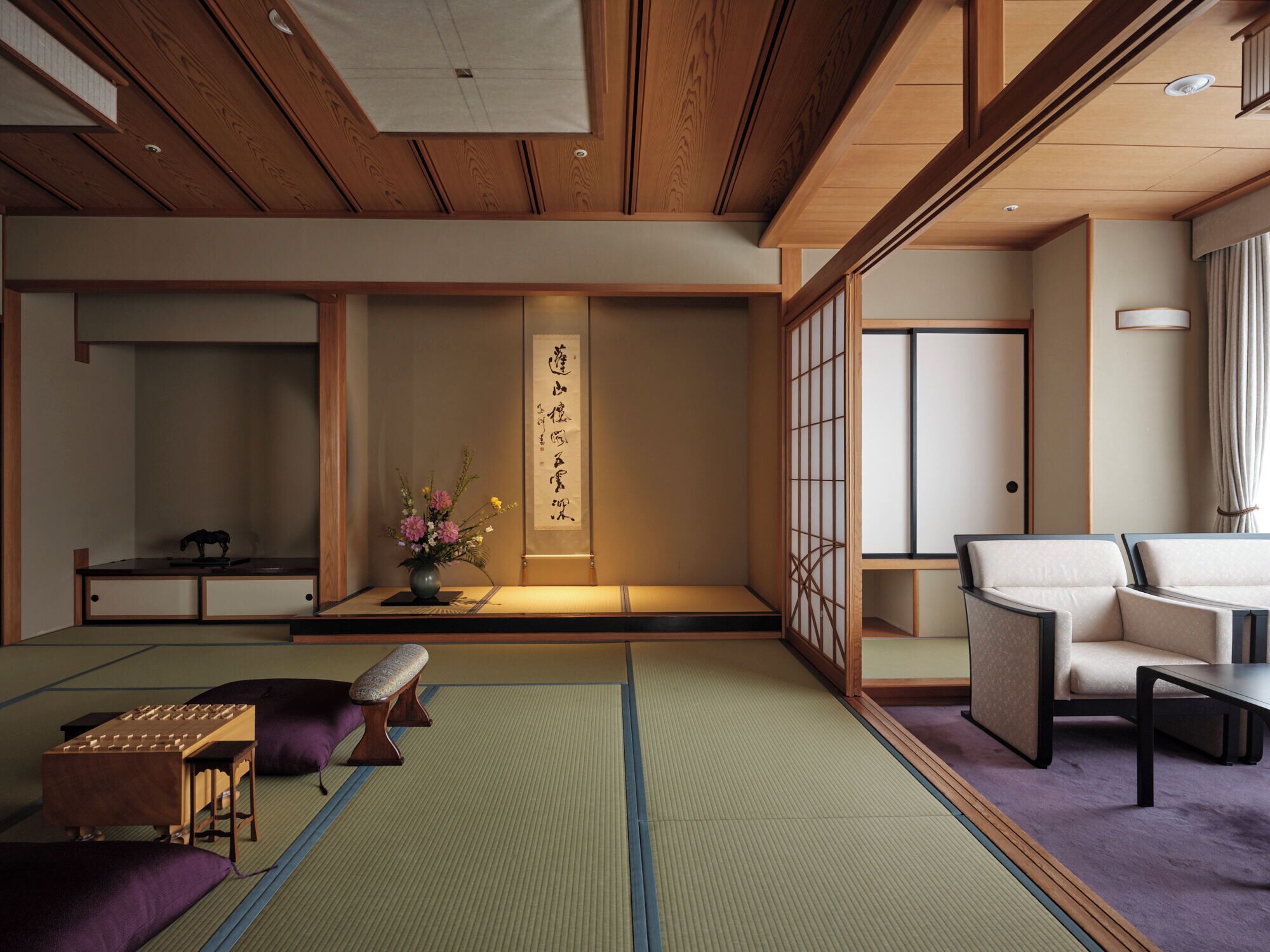 Una habitación tradicional japonesa con suelo de tatami, una mesa baja con un jarrón de flores y un puertas correderas con caligrafía.
