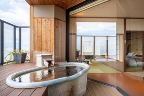 Un interior moderno con una bañera de hidromasaje de piedra, terraza de madera y vistas a la ciudad.
