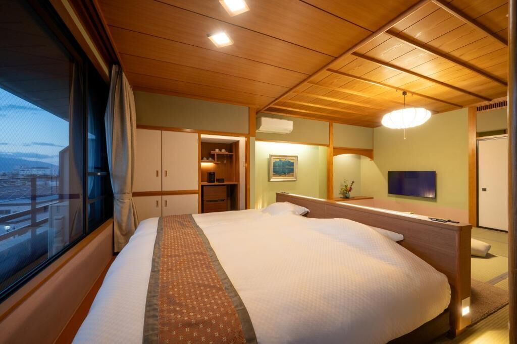 A hotel room with a large bed, wooden ceiling, a TV, and a window with a view.