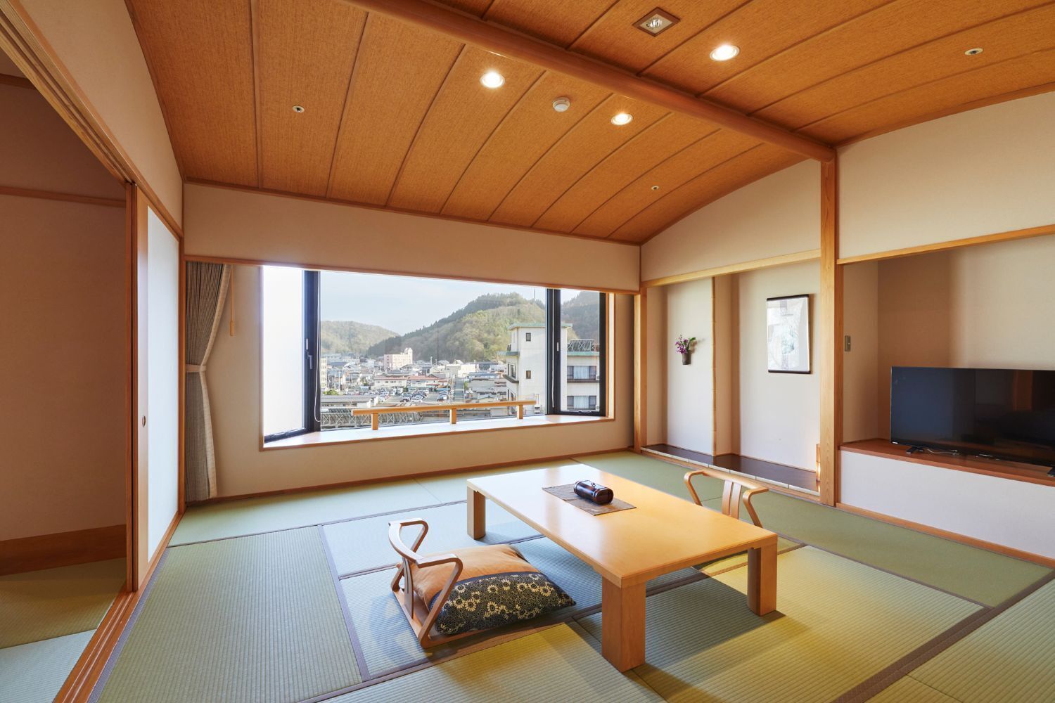 A traditional Japanese room with tatami flooring, a low wooden table, a sofa, and a TV.