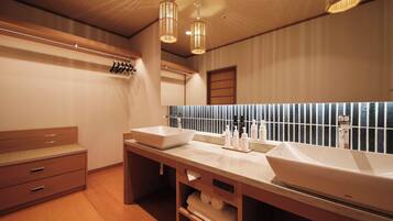 A modern bathroom with a large mirror, two sinks, wooden cabinets, and a towel rack.