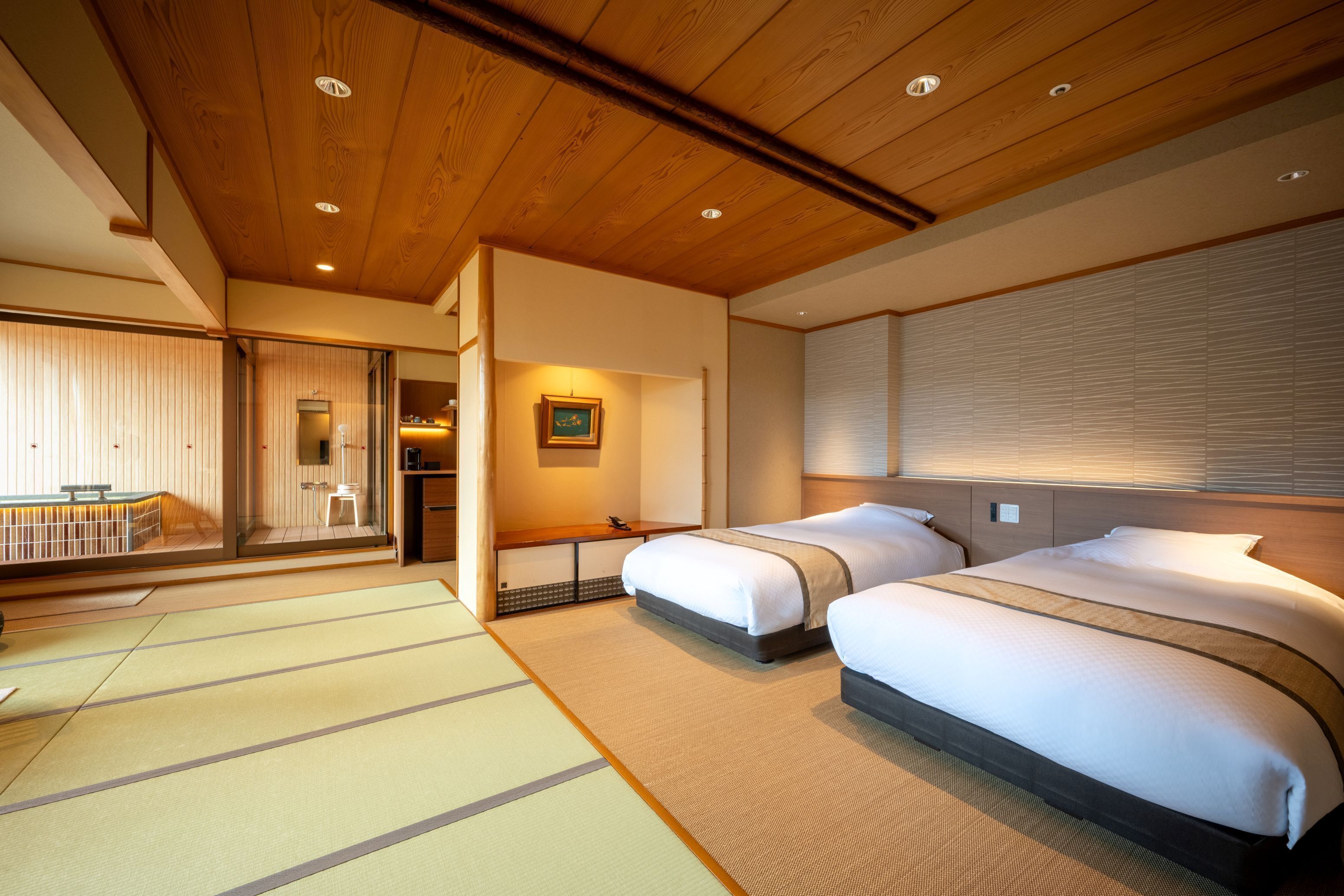 Quarto de hotel com duas camas, piso de esteira de tatame, teto de madeira e porta deslizante para uma varanda.