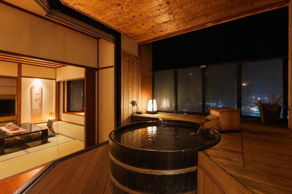 A hot tub on a wooden deck with a view of the city at night.