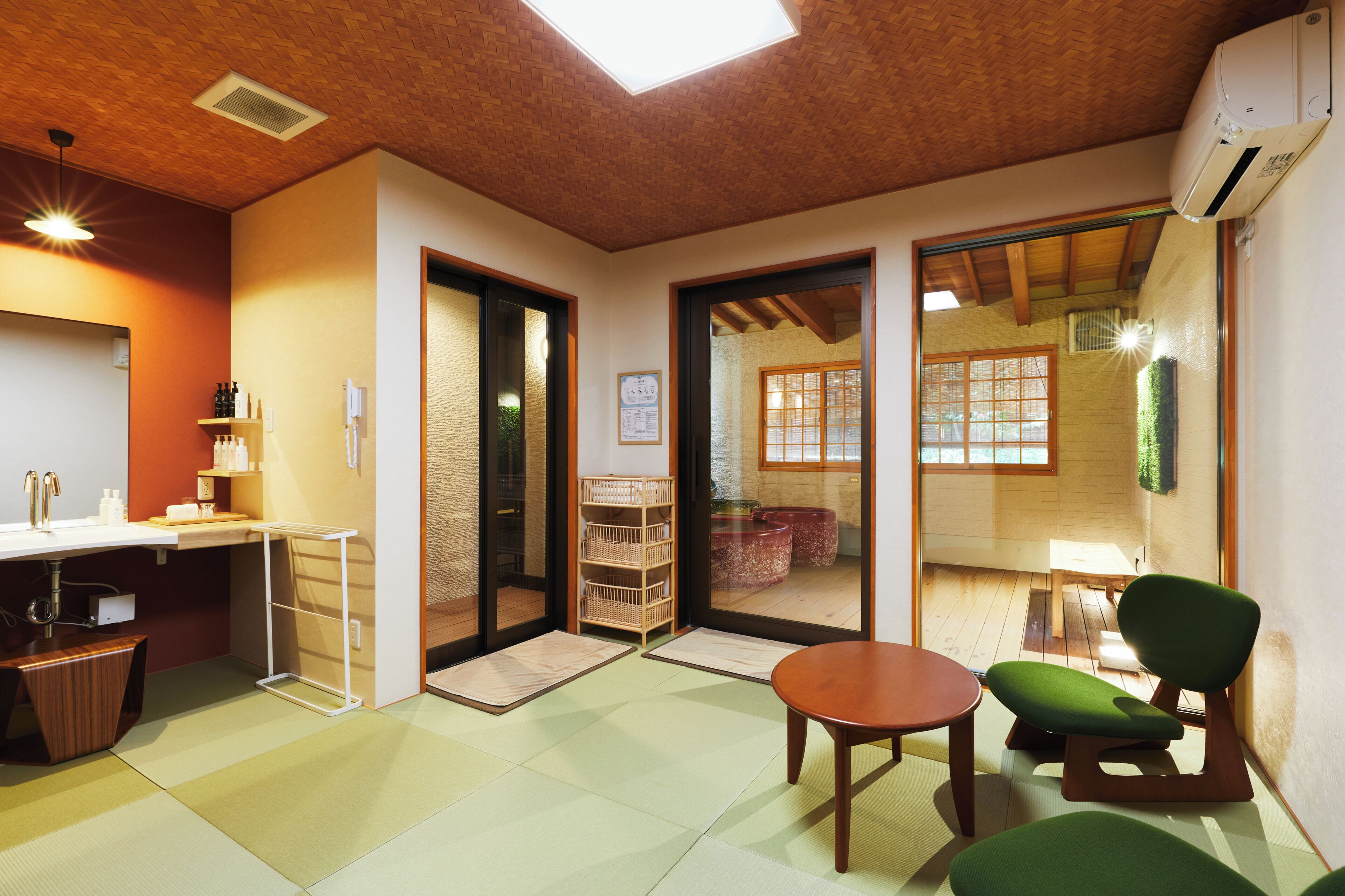 A traditional Japanese room with tatami flooring, a low table, a green chair, and sliding doors leading to a view of a garden.