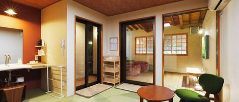 A traditional Japanese room with tatami flooring, a low table, a green chair, and sliding doors leading to a view of a garden.