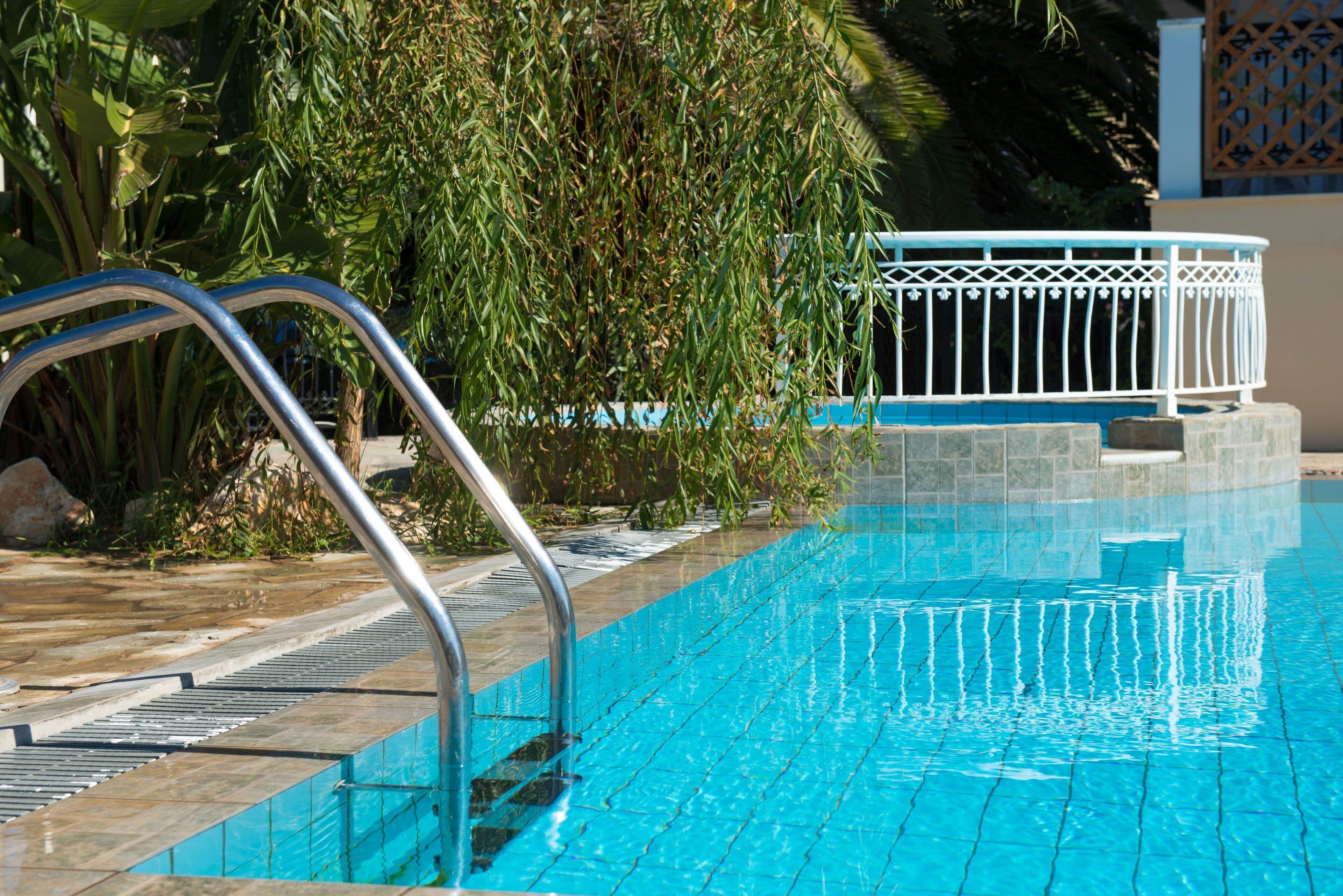 Una piscina con agua azul cristalina, una escalera metálica y una estructura blanca junto a la piscina.