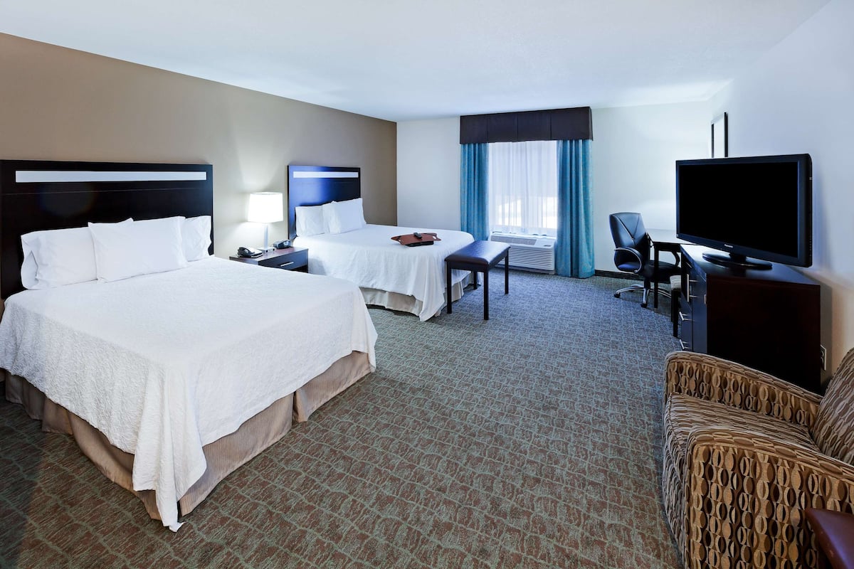 A hotel room with two beds, a desk, a chair, a television, and a window with curtains.
