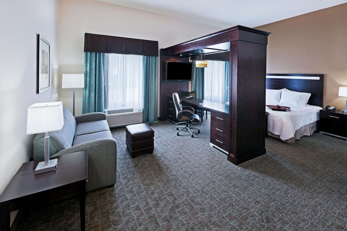 A hotel room with a bed, a desk, a chair, a television, and a window with curtains.