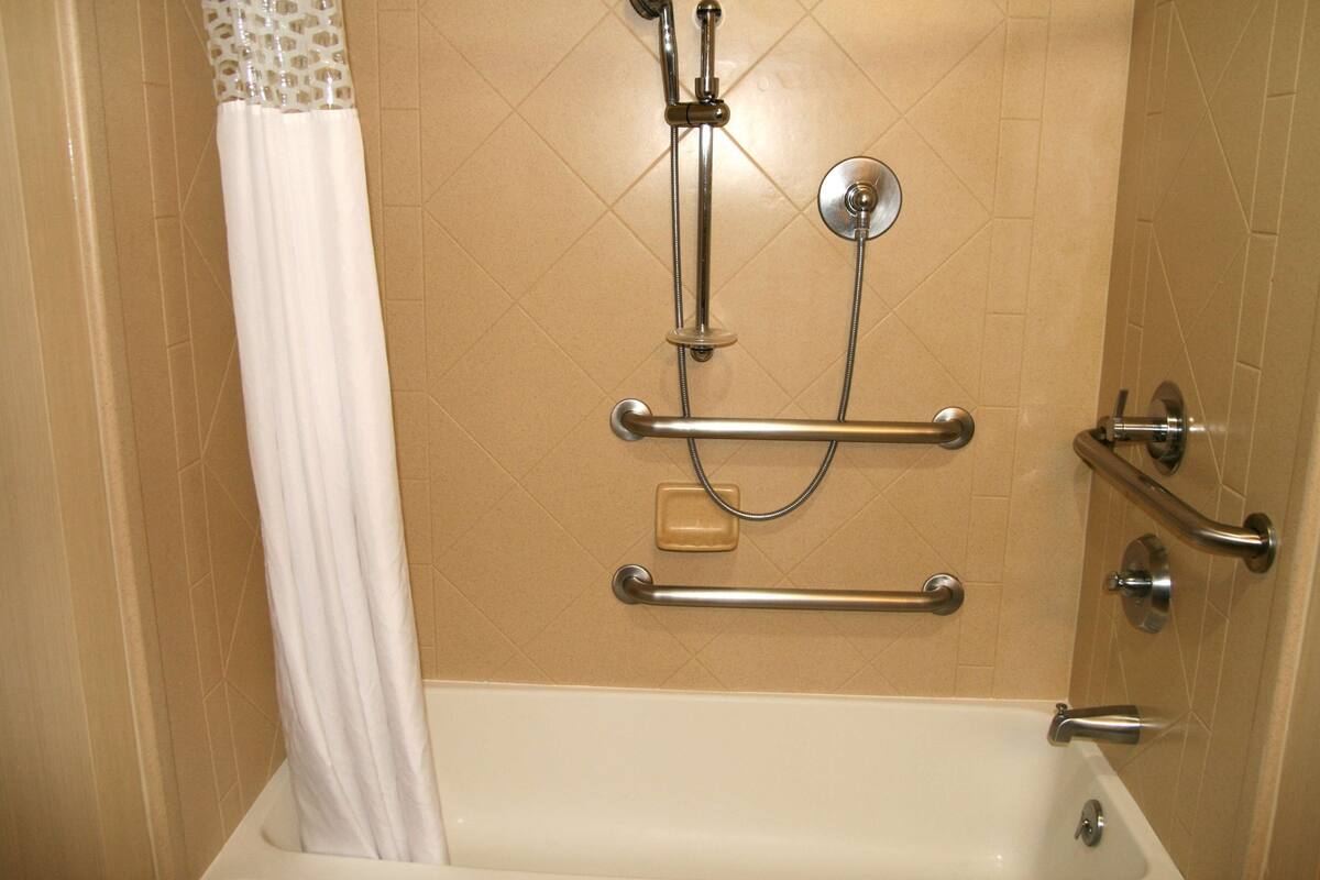A bathroom with a bathtub, grab bars, a showerhead, and a curtain.