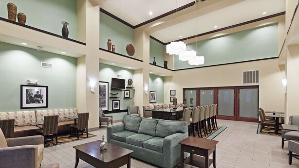 Eine geräumige Lobby mit einem grünen Sofa, mehreren Sitzbereichen, einem Fernseher und einer Rezeption.