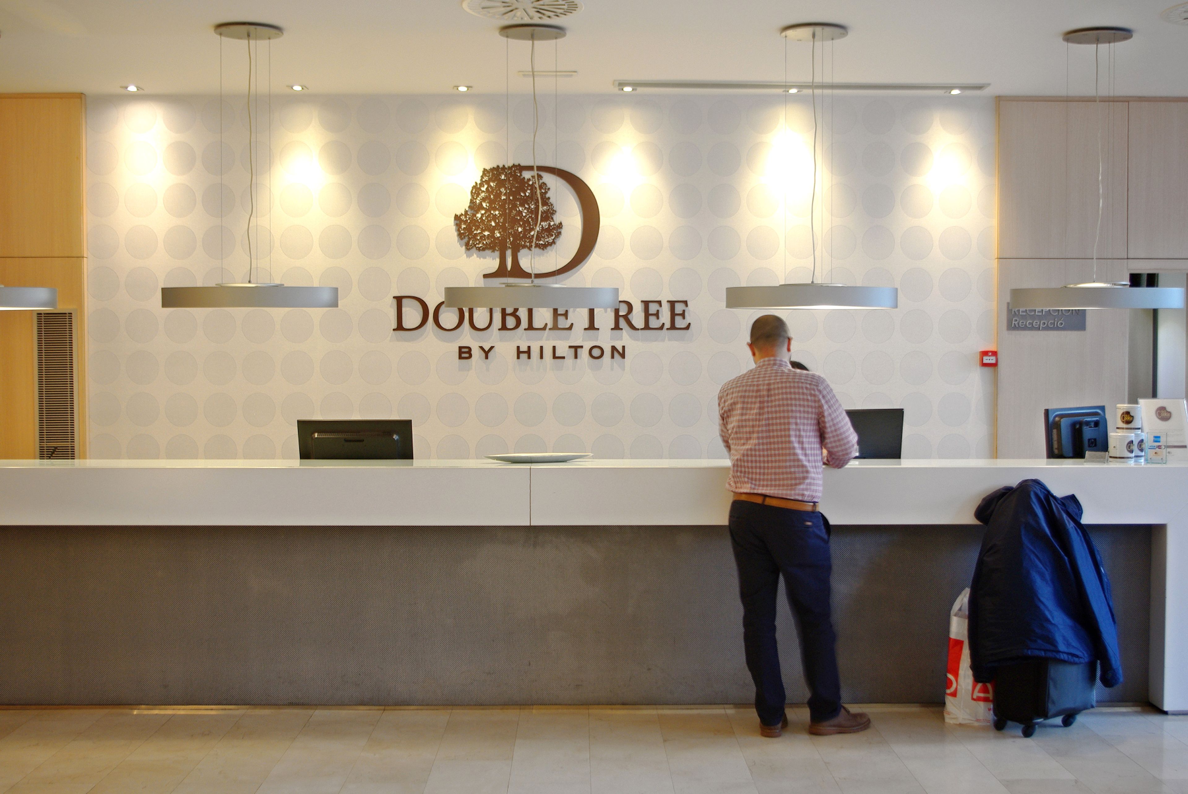 Een receptiebalie met een logo, een man die erachter staat, en een bordje dat een receptiezone aangeeft.