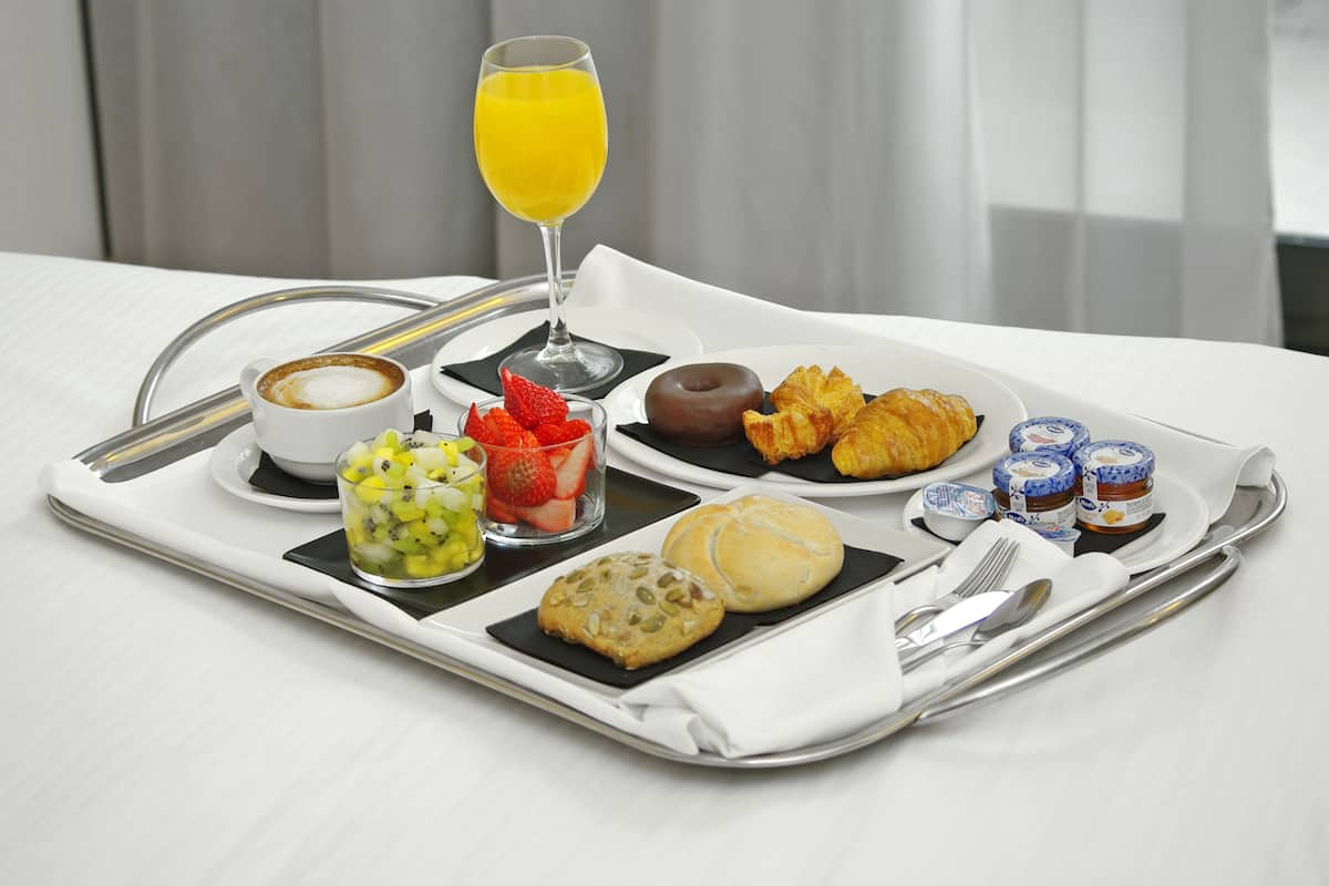 A breakfast tray with a croissant, cookie, fruit, and a glass of orange juice.
