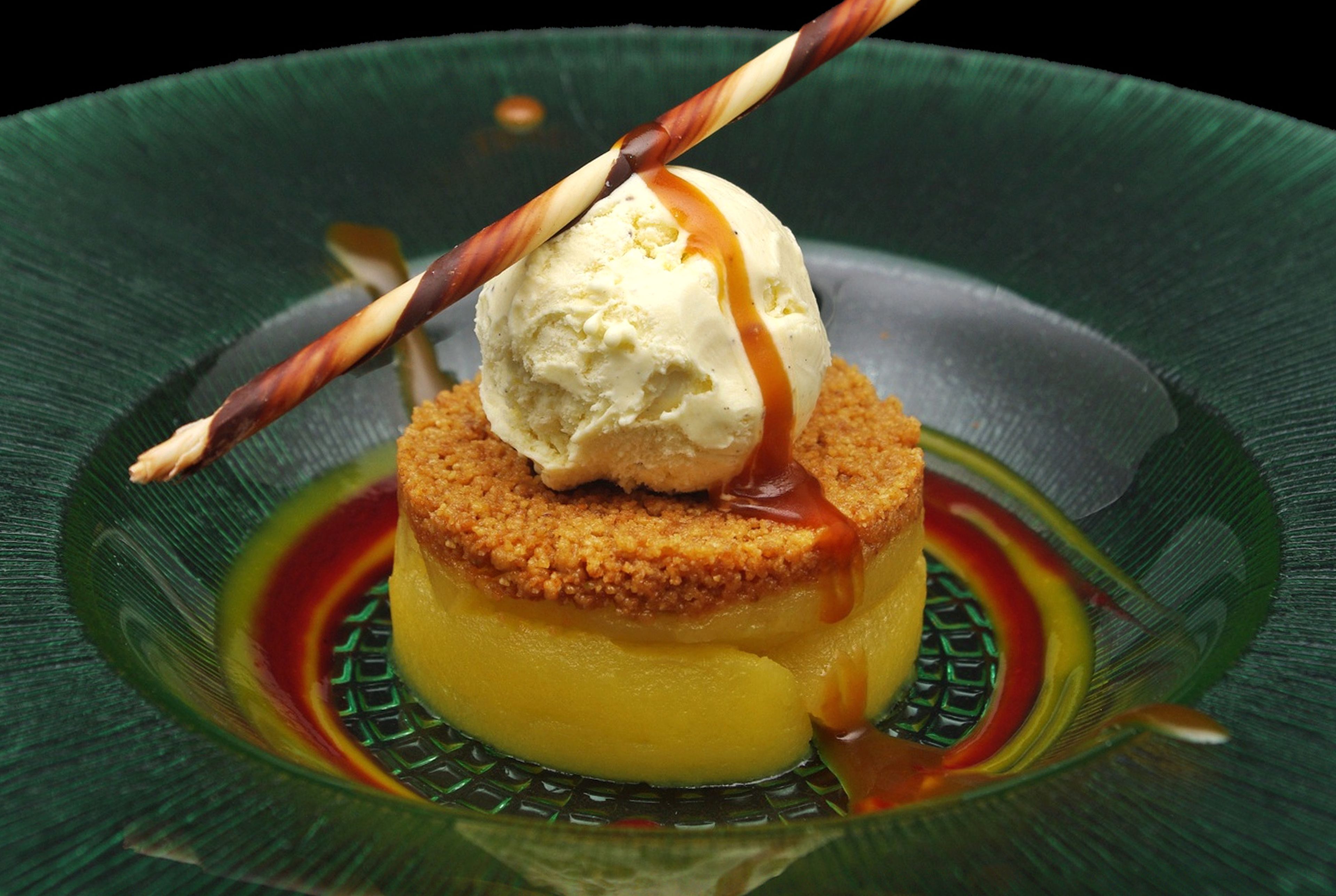 Un postre con una porción de helado sobre una base caramelizada, servido en un plato verde.