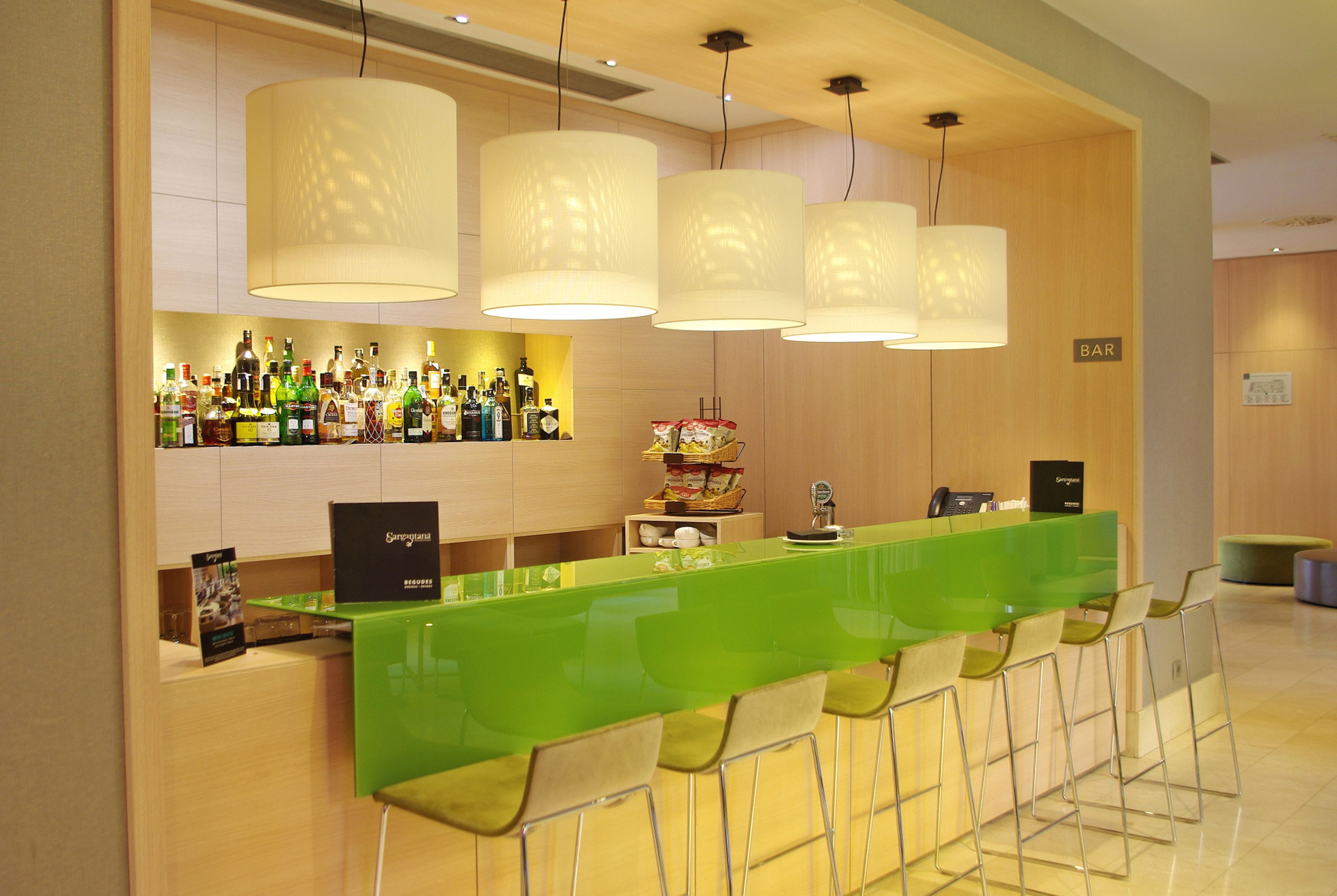 A bar area with a green counter, multiple hanging lamps, and a variety of bottles.