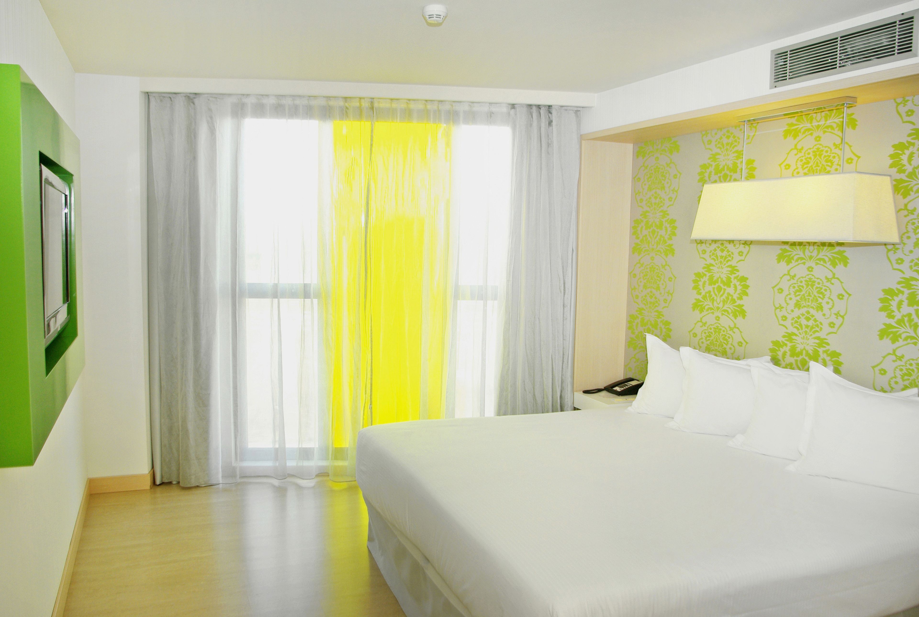 Habitación de hotel con una cama grande, una mesita de noche, una lámpara, un teléfono y una ventana con cortinas.