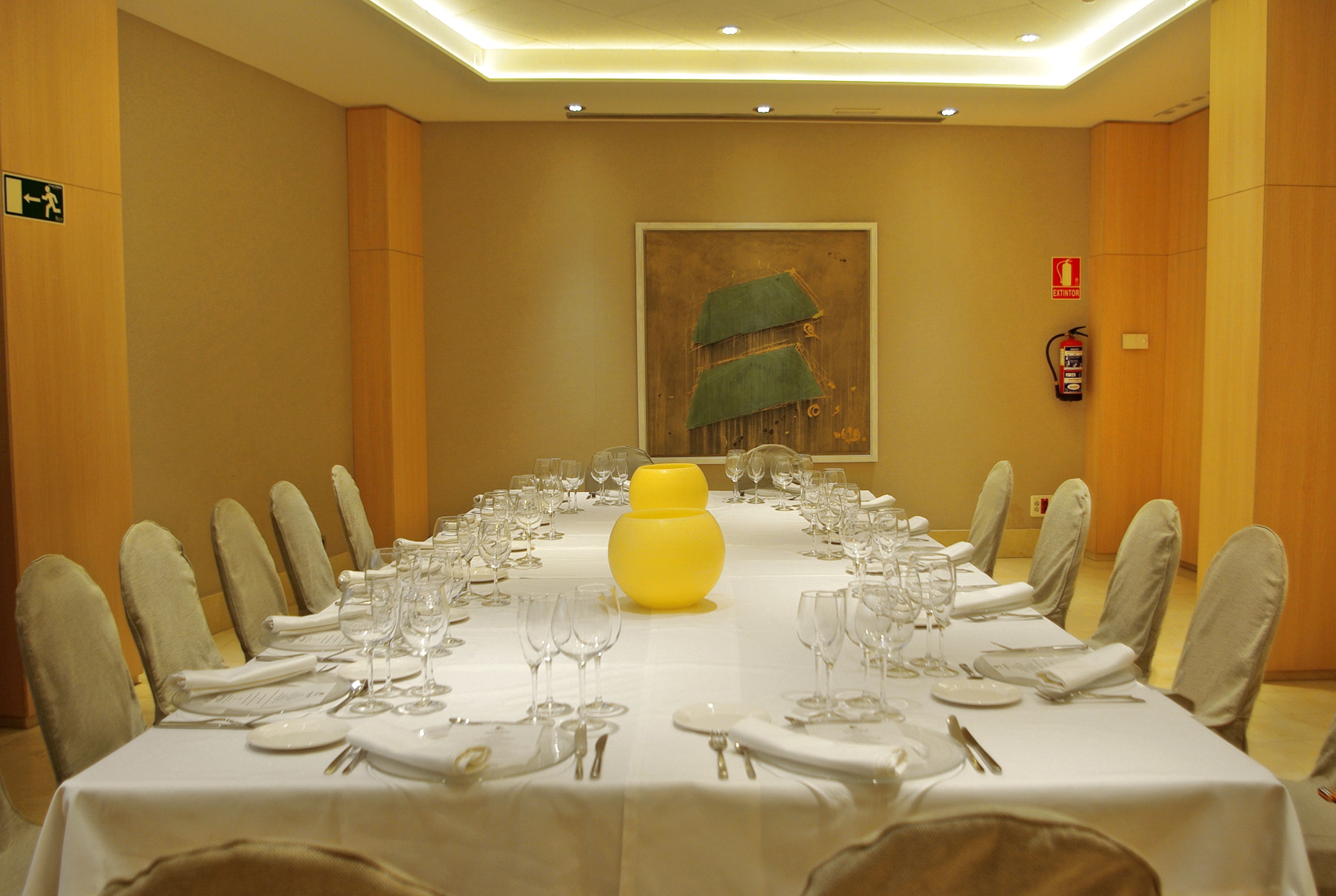 Sala de conferências com uma mesa comprida posta para uma reunião, equipada com cadeiras e um centro de mesa amarelo.