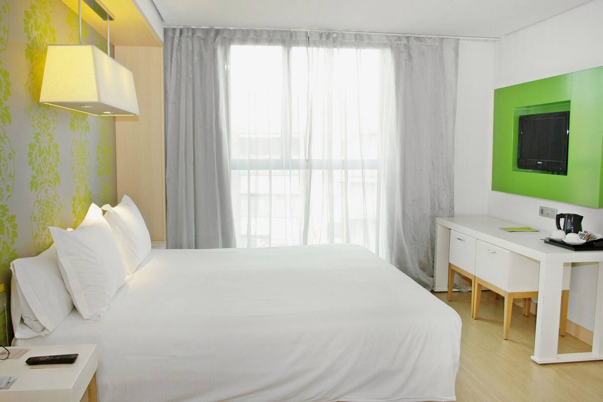 A hotel room with a large bed, a desk, a television, and a window with curtains.