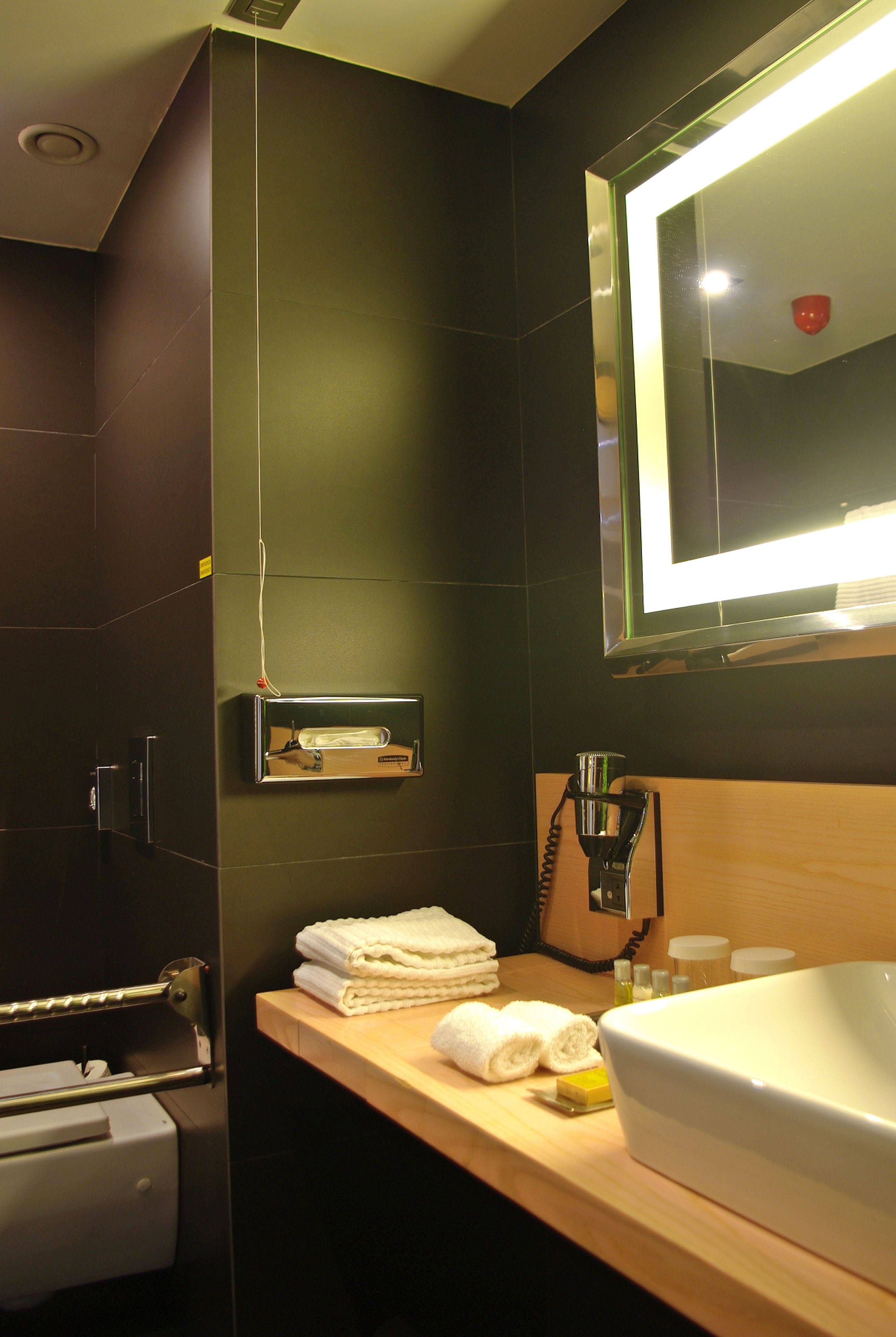 A modern bathroom with a large mirror, a sink, and a towel dispenser.
