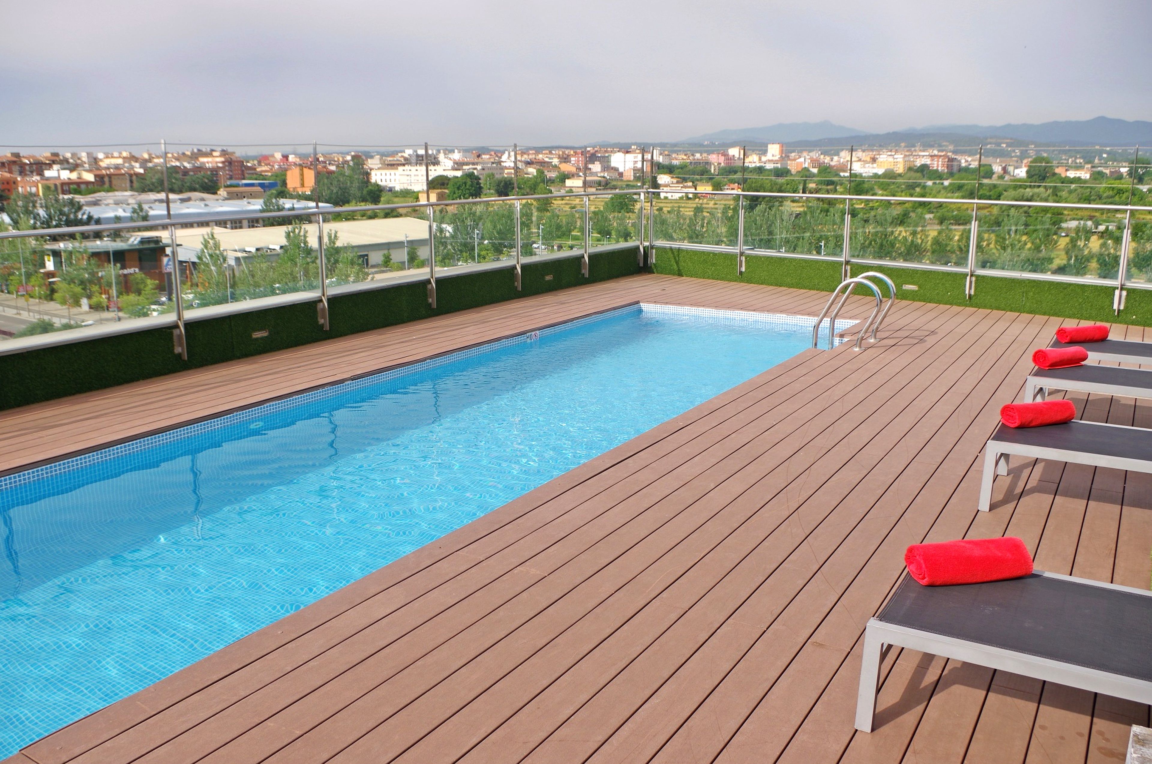 A rooftop pool with wooden deck and lounge chairs.