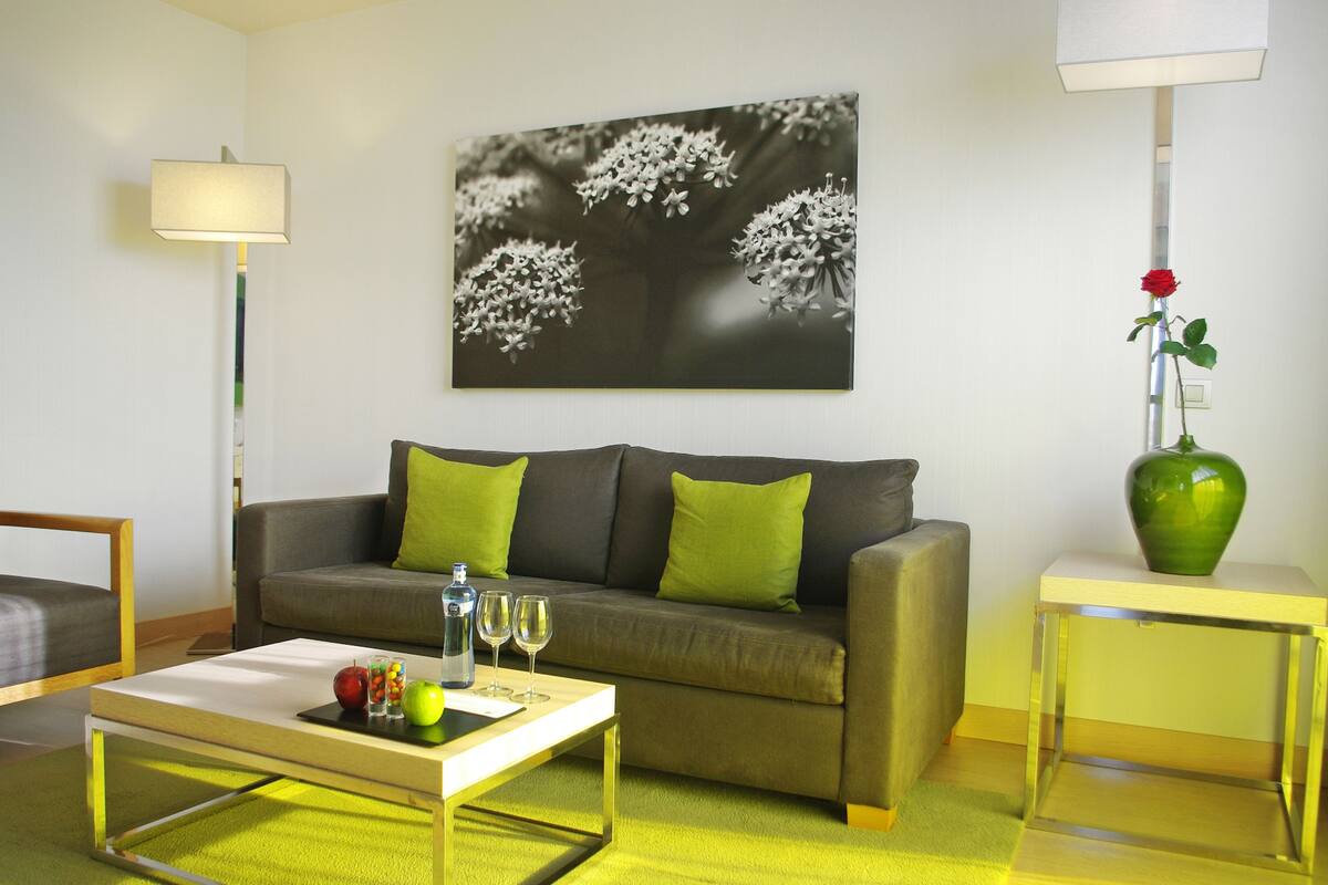 A living room with a sofa, a coffee table, a lamp, and a vase with a rose.