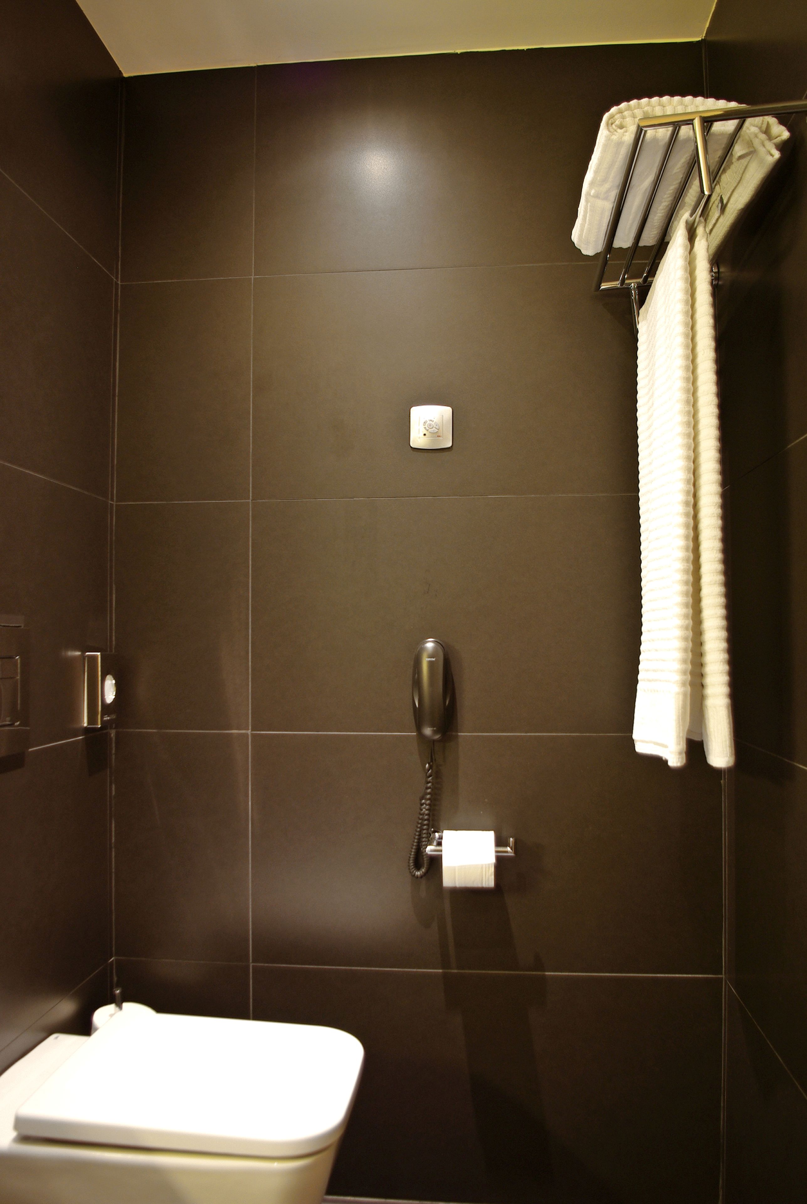 A modern bathroom with dark tiles, a toilet, a towel rack, and a telephone.