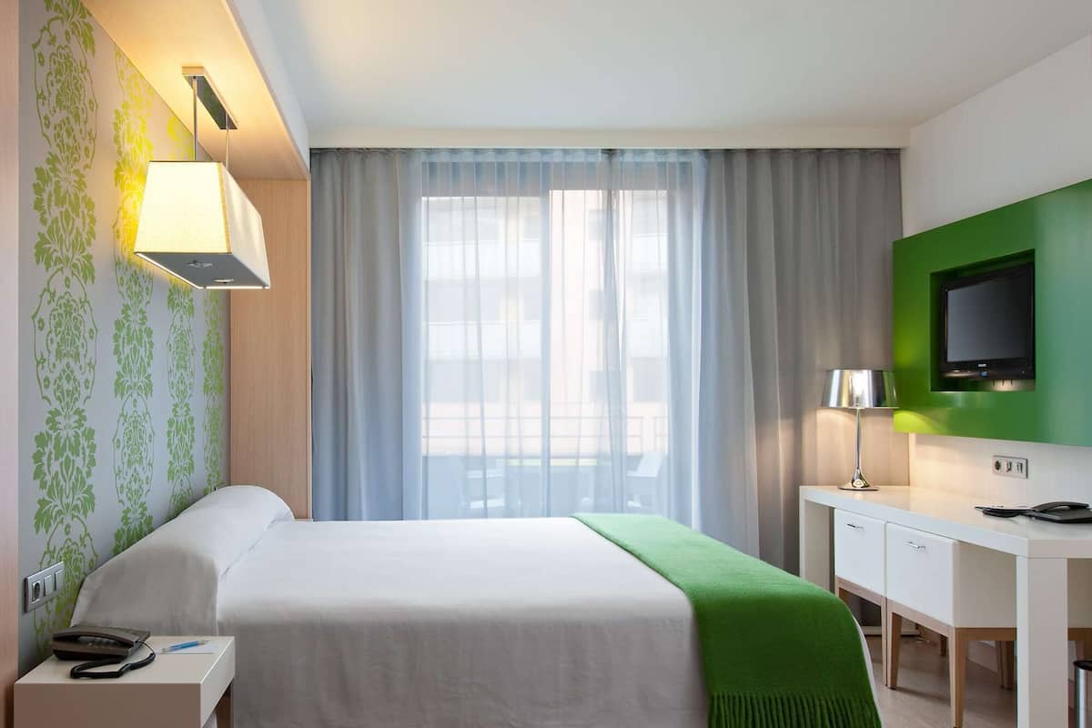 A hotel room with a bed, bedside table, desk, and a television.
