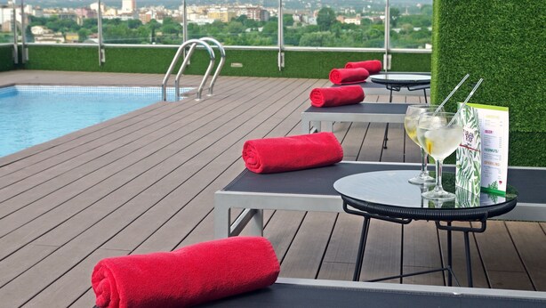 A rooftop pool area with a view of a cityscape, including a swimming pool, lounge chairs, and a table with drinks and a menu. - DoubleTree by Hilton Hotel Girona (Girona)