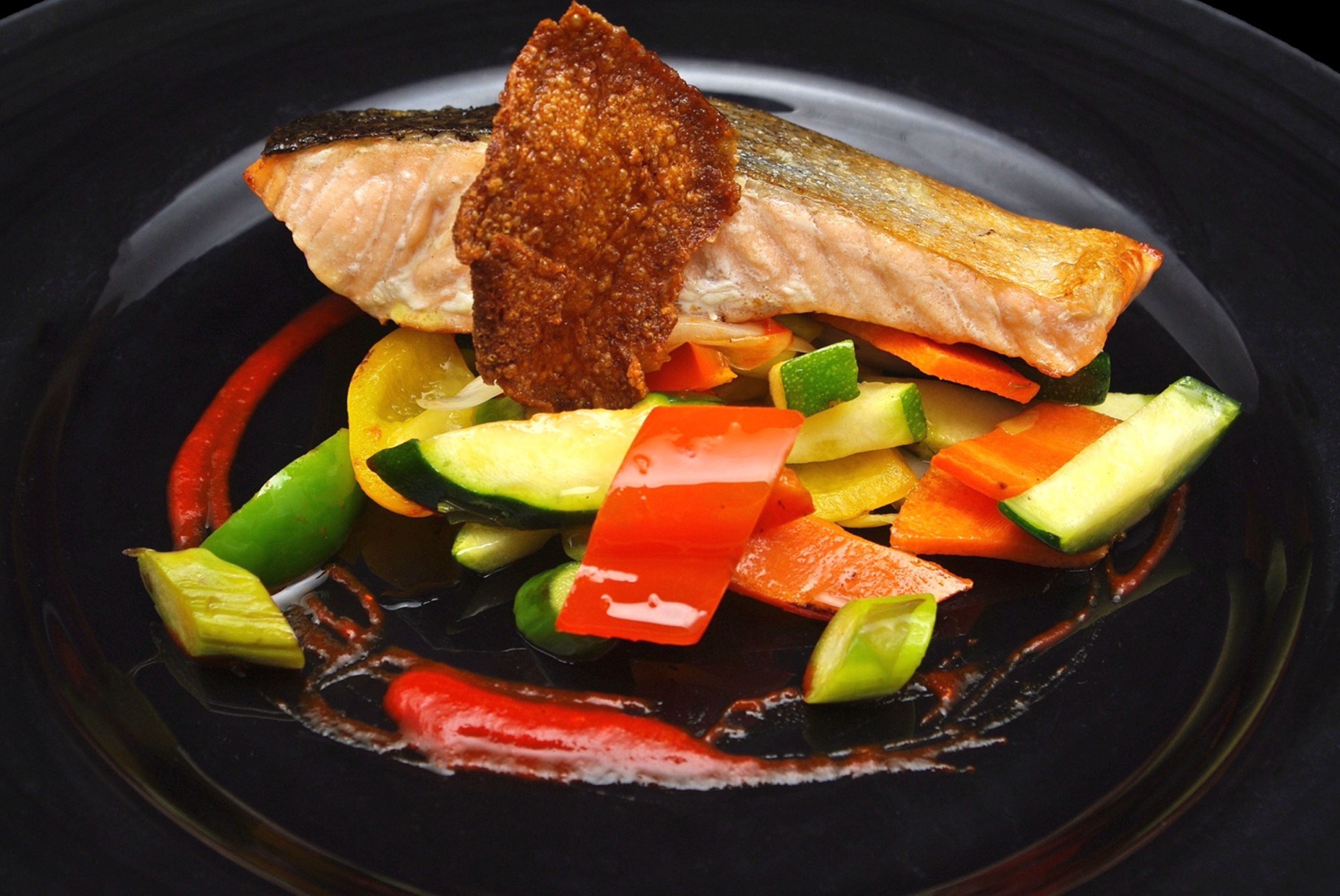 Un plato con salmón, verduras y salsa.