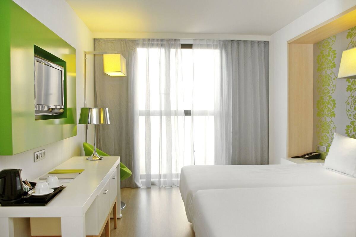 Habitación de hotel con cama, escritorio, cafetera, lámpara y televisión.