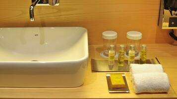 A hotel bathroom with a large white sink, a mirror, and toiletries including bottles of lotion and a bar of soap.