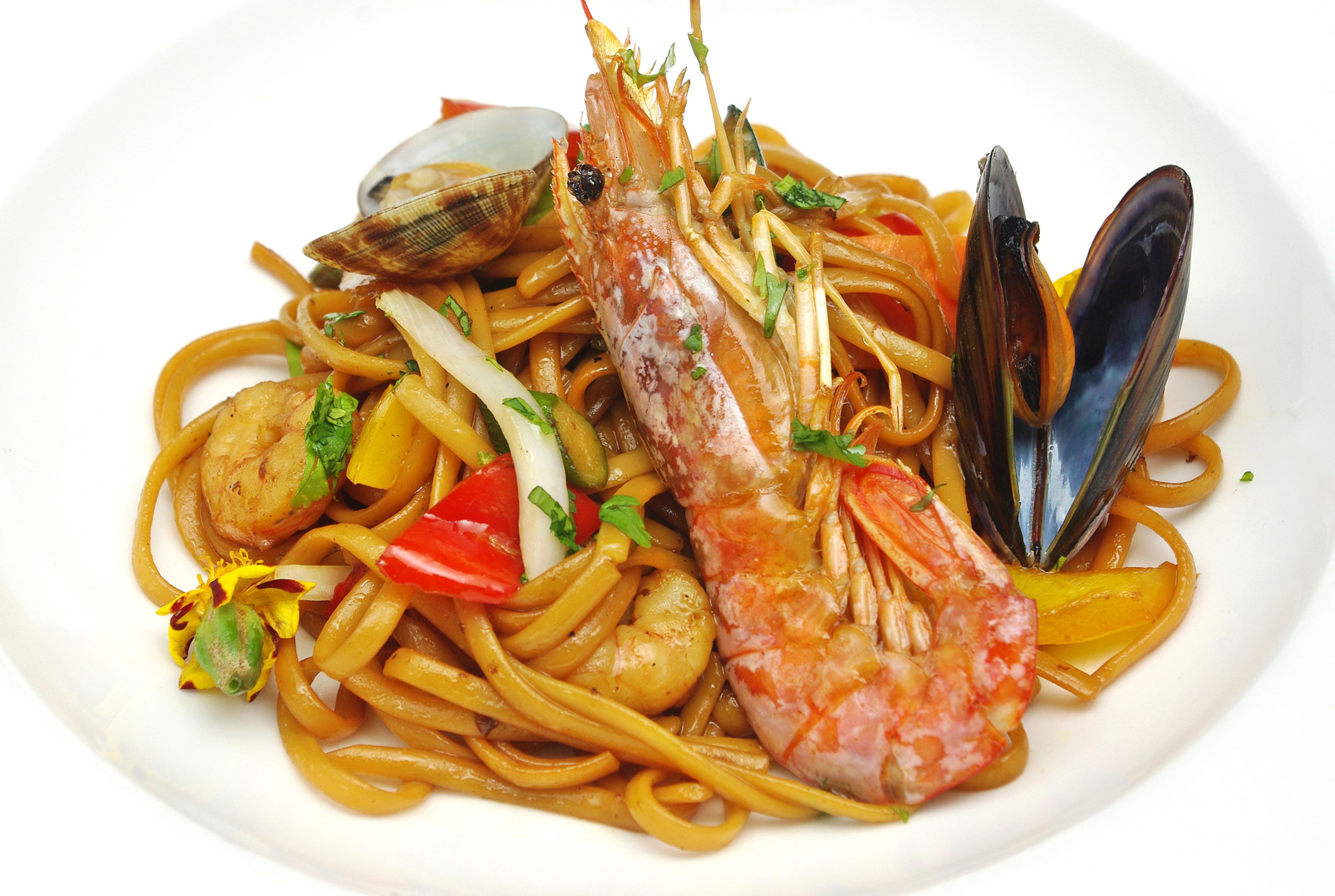 A plate of seafood pasta with shrimp, mussels, clams, and vegetables.